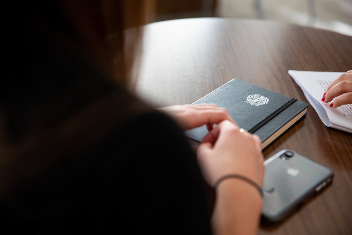 Person sitting at desk with a notebook and phone on the table.