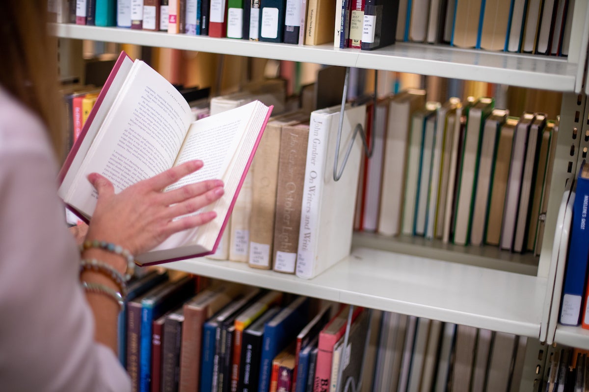 Person reading a book in front of a shelf of other books.