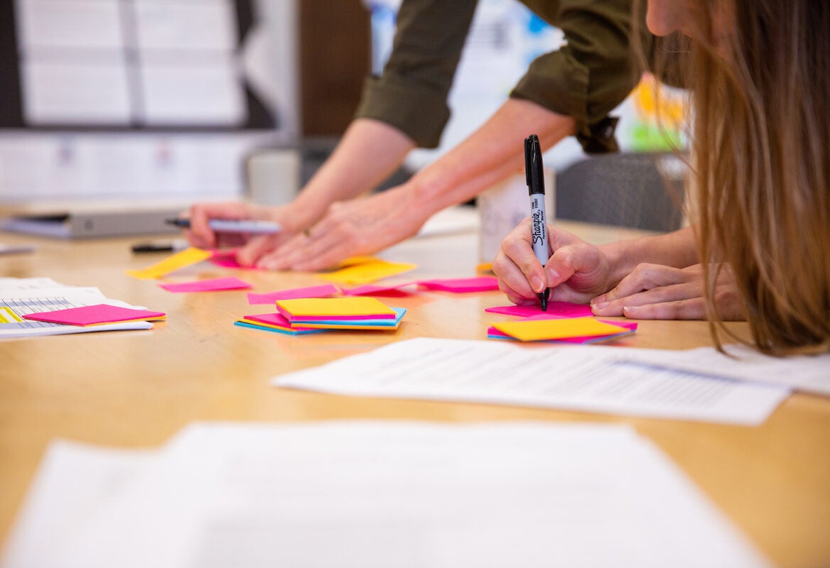 Two people writing on sticky notes on a desk.